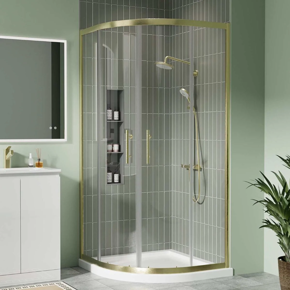 Brushed brass quadrant shower enclosure with sliding glass doors and white shower tray in a modern green-tiled bathroom.